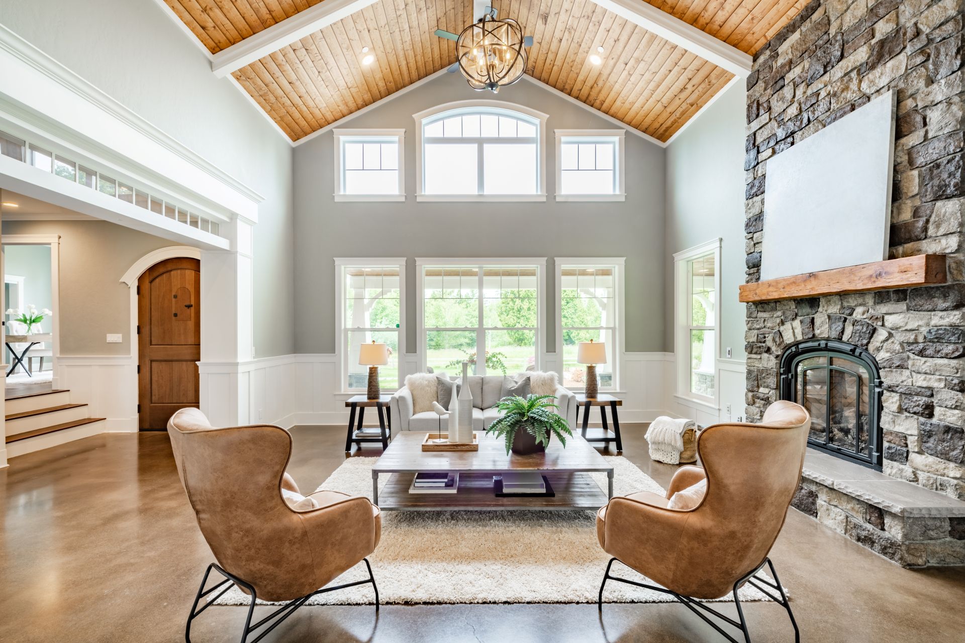 Living room interior with vaulted ceiling with wood cedar panelling stone fireplace brown leather armchairs coffee table and area rug natural brown tones