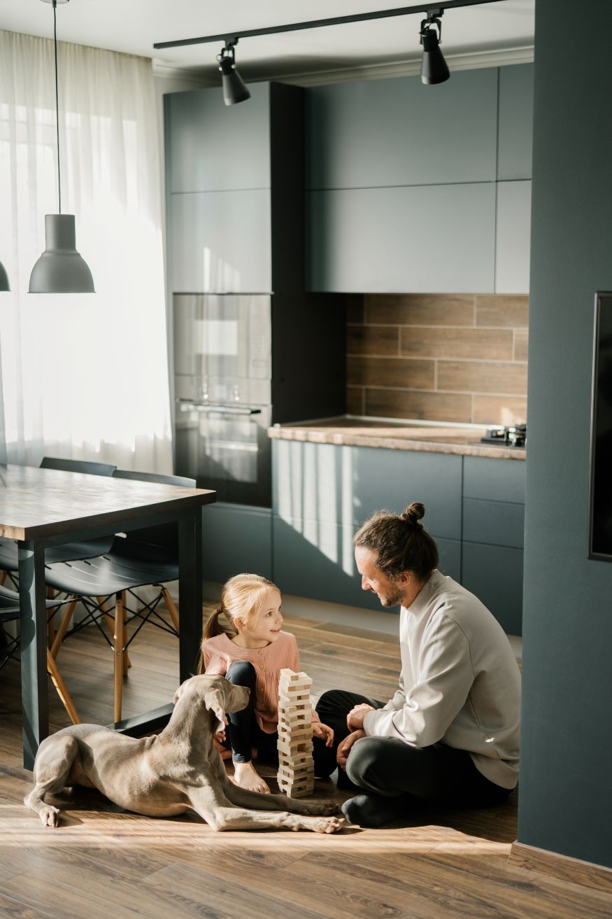 Dad and daughter are playing a board game in the kitchen, sitting on the floor. A dog is lying nearby. Scandinavian and high-tech style in the interior. Family leisure