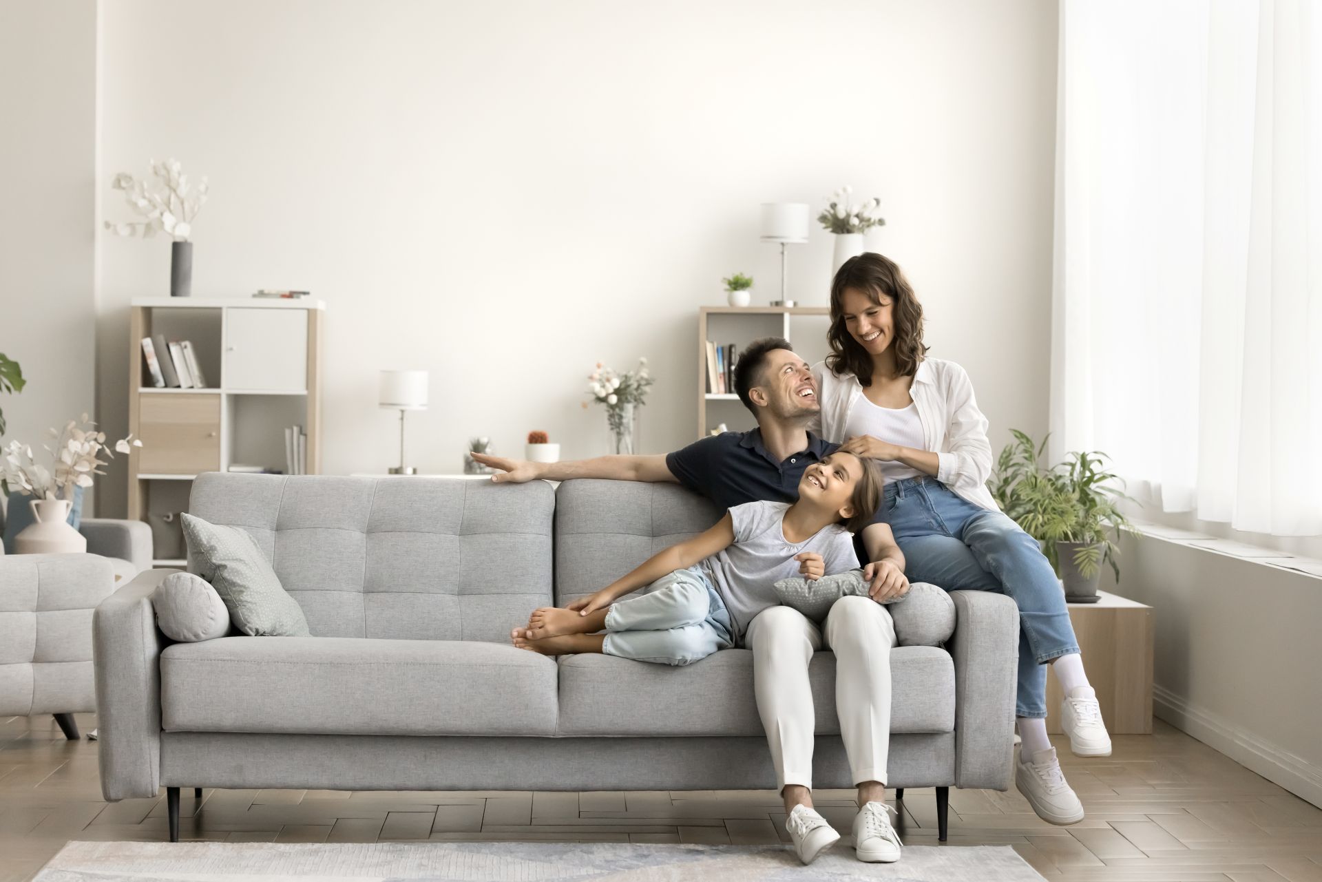 Happy couple of young parents and little daughter kid sitting and relaxing on sofa, resting on comfortable couch in modern cozy home interio