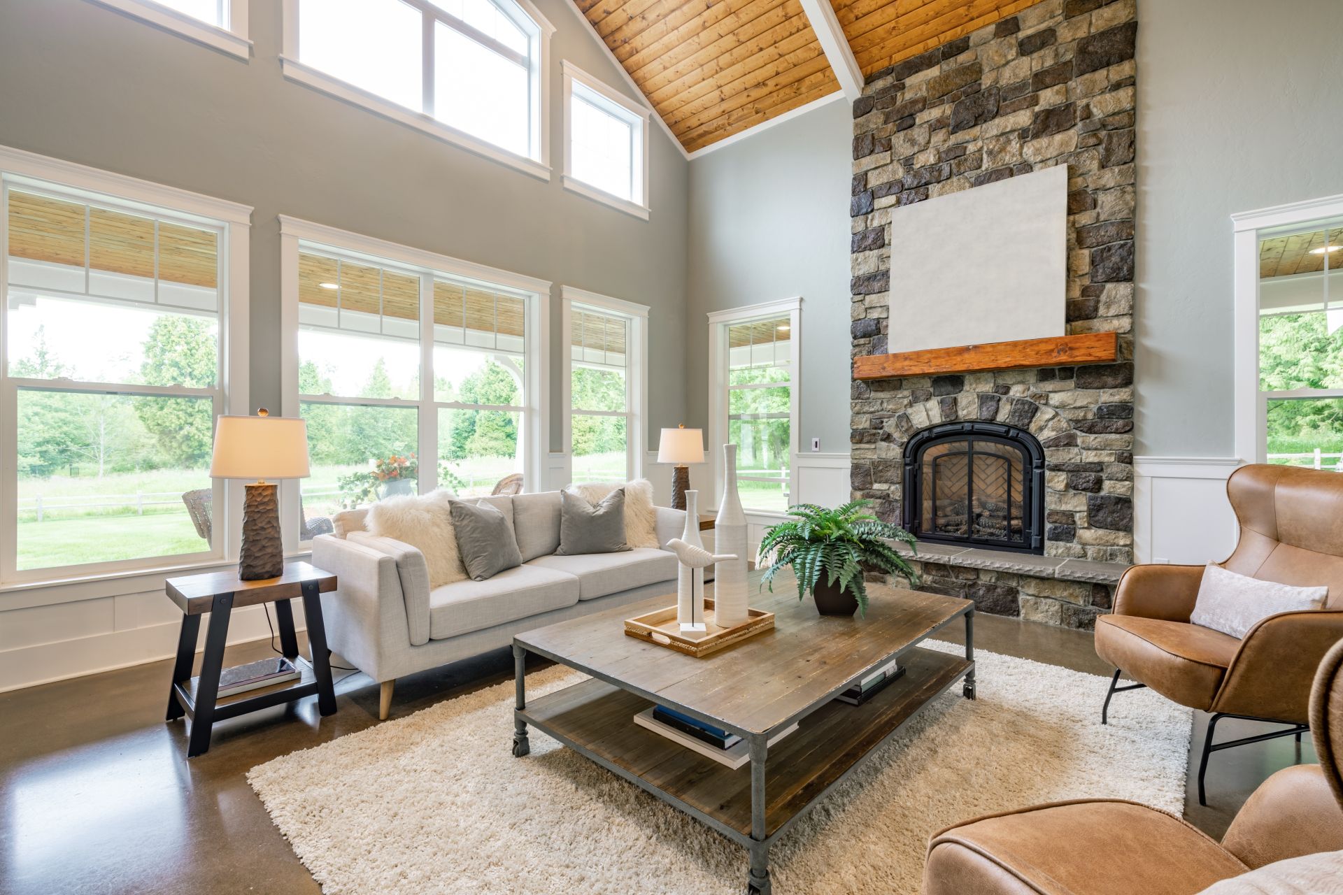 Living room interior with wooden beams hardwood flooring area rug furnishings sofa fireplace cabinets bohemian style houseplants arm chairs in natural colors