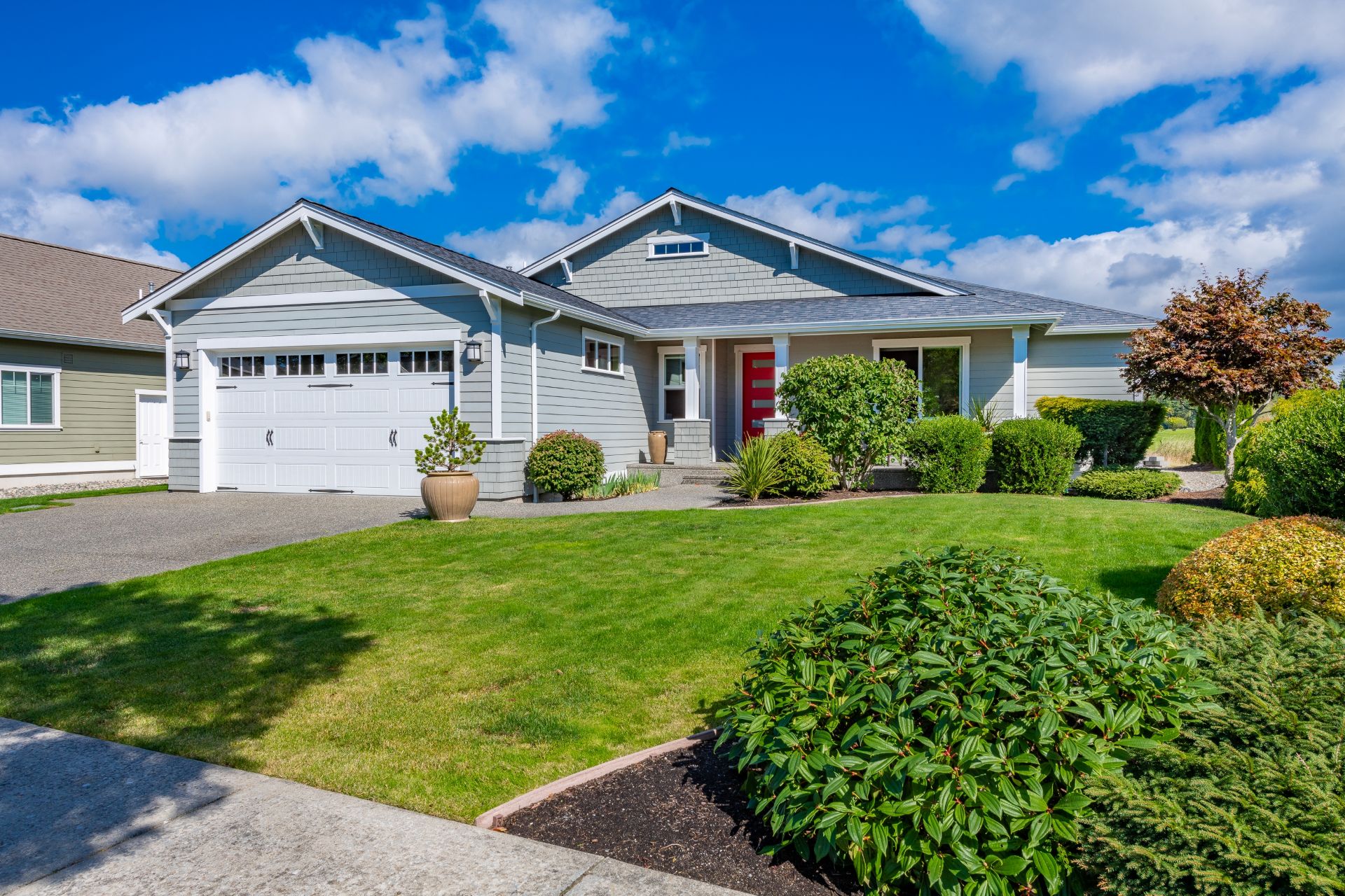 exterior of a single level home with blue sky grey front red door and green grass