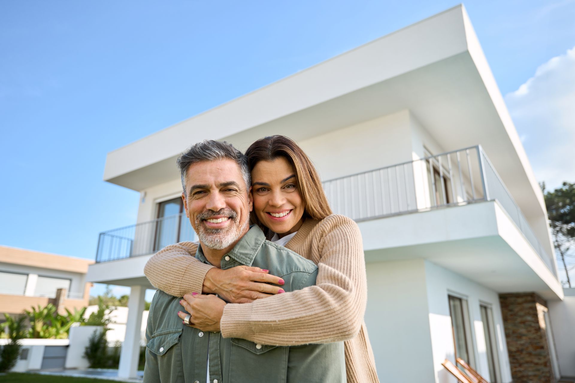 Happy smiling mature older family couple new property buyers modern dream luxury villa owners standing outside house,