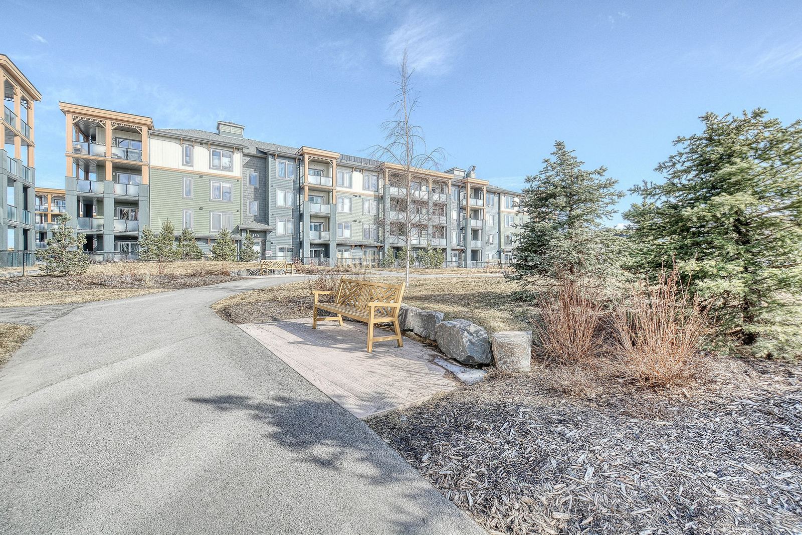 Paved pathway with a bench beside condo buildings in Auburn Bay, southeast Calgary
