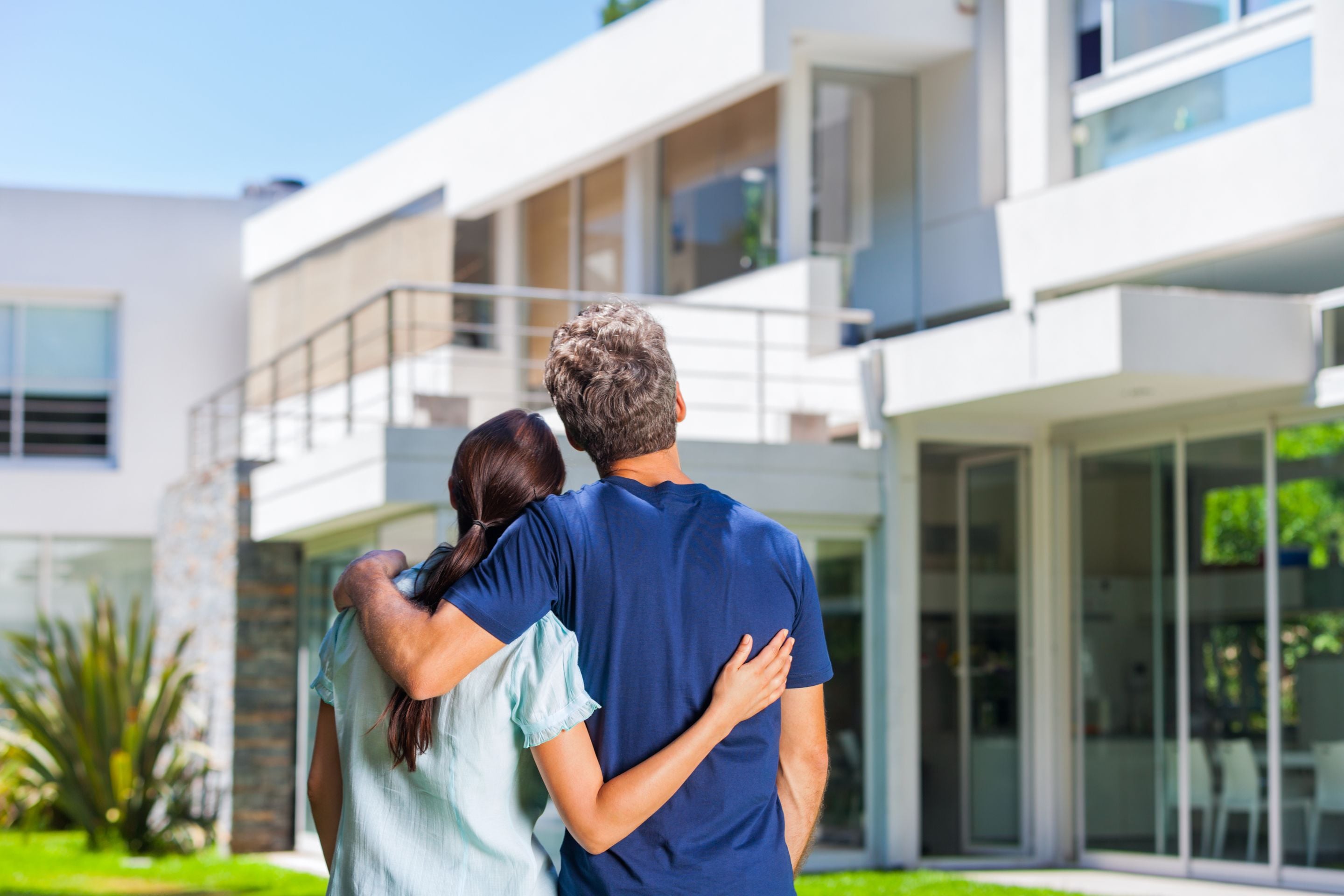 couple embracing in front of new big modern house, outdoor rear view back looking at their dream home (1)