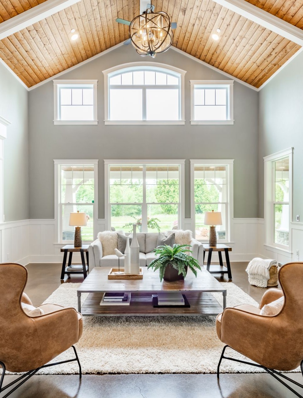 Living room interior with vaulted ceiling with wood cedar panelling stone fireplace brown leather armchairs coffee table and area rug natural brown tones vert