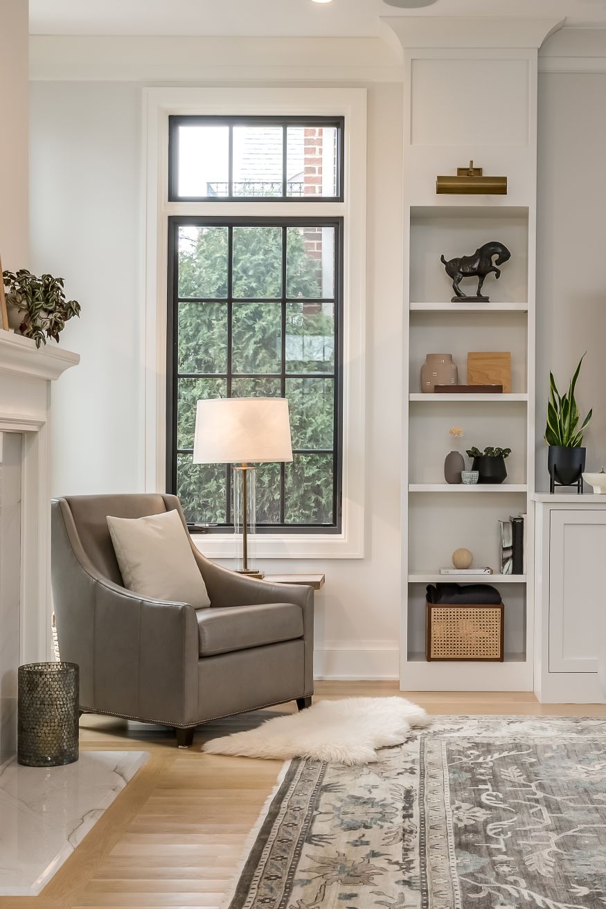 Transitional Interior Design Living Room Aesthetic. Gray side chair near window with neutral styling on shelves. Gray area rug with potted plants.