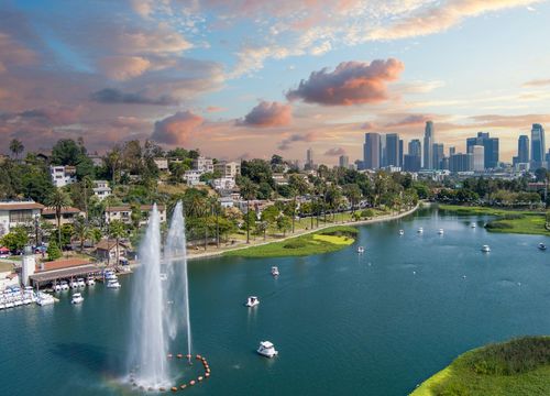 aerial shot of the skyscrapers, office buildings and hotels in the city skyline, a lake with people in pedal boats, green trees and grass, powerful clouds at sunset in Los Angeles California USA