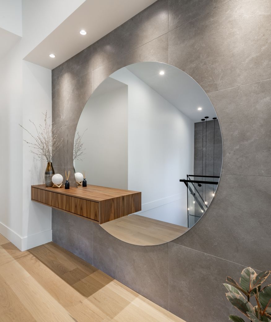 Contemporary home interior staircase cantilever steps glass panel wrought iron hardware hallway with built in cabinet large round mirror large windows wooden floor bright modern spacious hall