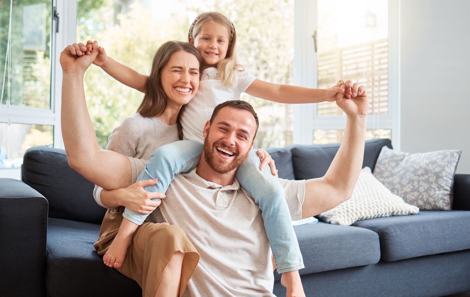 Smile, family and portrait on shoulder by sofa for weekend fun, happiness and bonding together. Playful, mom and dad with daughter in living room for support, care and love at home on fathers day (1)