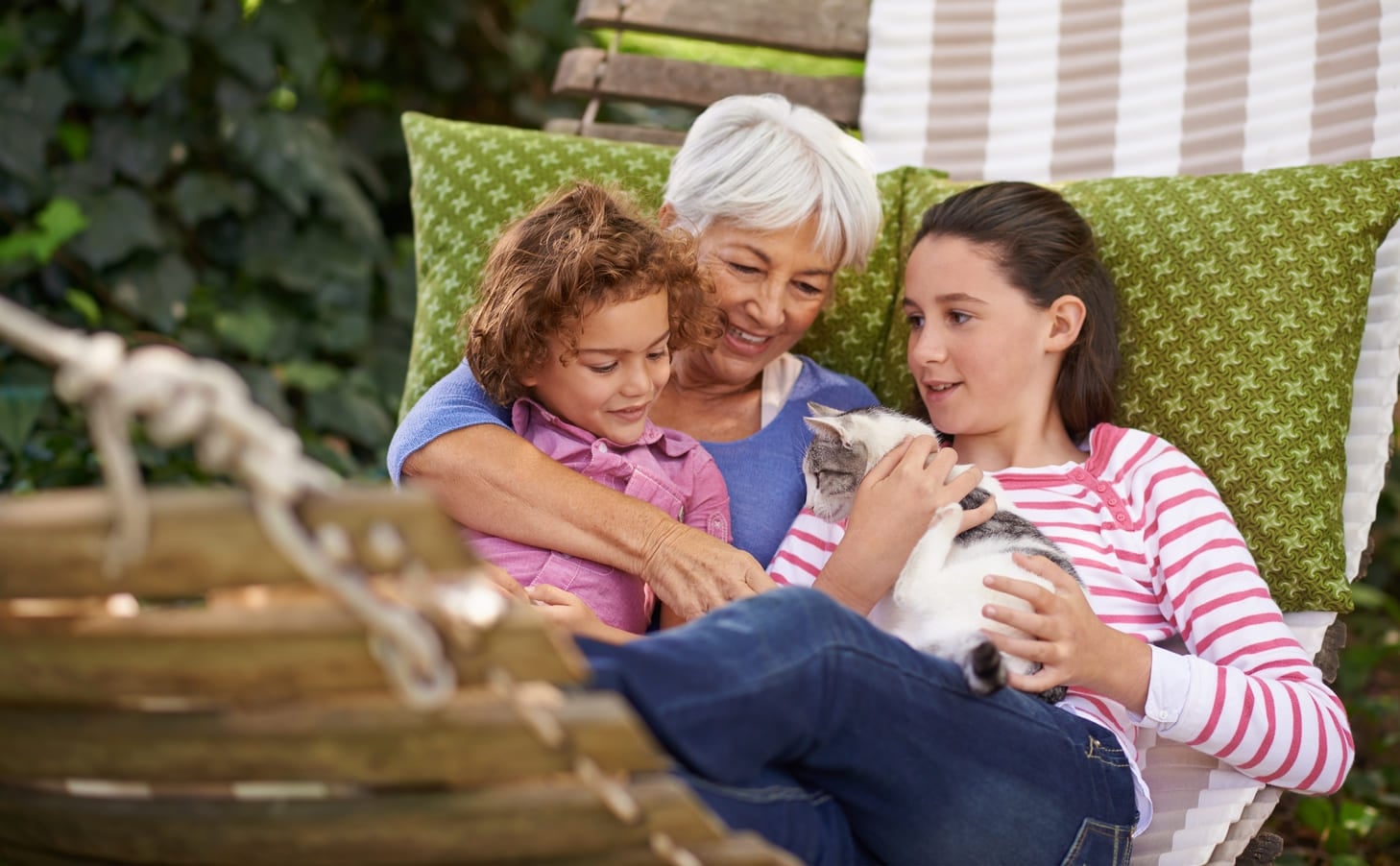 Everyone loves a visit with Grandma. Shot of a grandmother and her grandchildren sitting outside on a hammock together with a cat.
