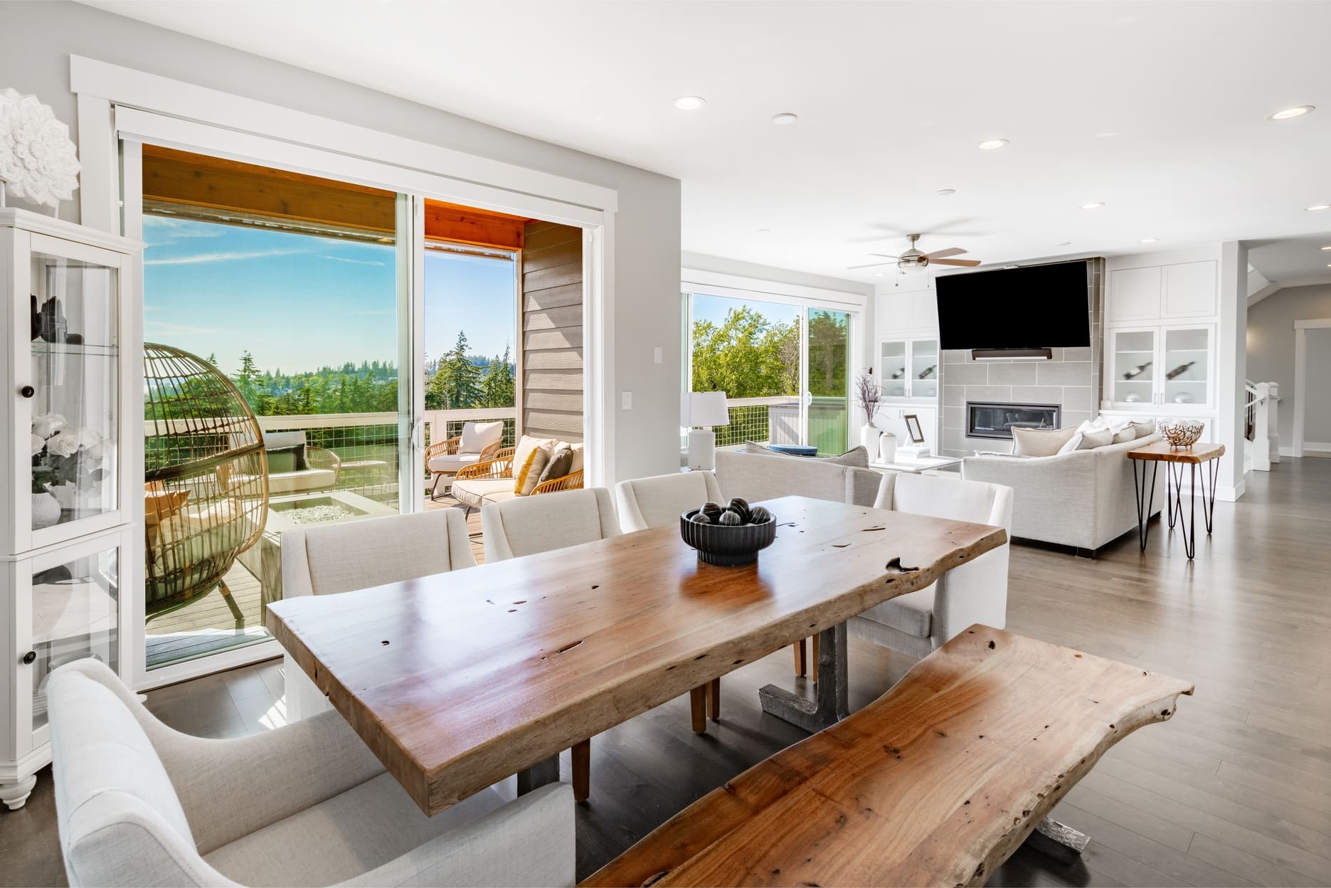 Interior living and dining room in a modern home with a view of the city and bay harbour ocean large open windows blue footstools decor staged comfortable dining table with bench