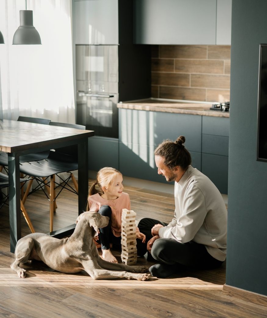 Dad and daughter are playing a board game in the kitchen, sitting on the floor. A dog is lying nearby. Scandinavian and high-tech style in the interior. Family leisure 1