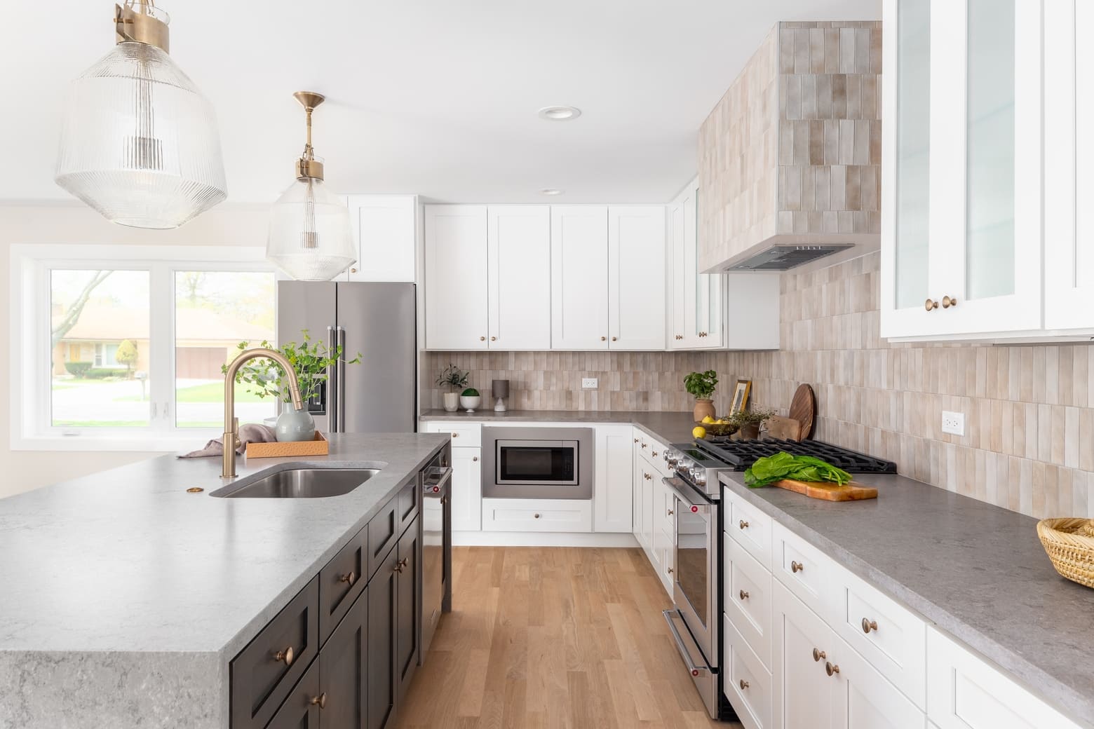 A white kitchen detail with stone countertops, gold light fixtures above the island, and a brown tiled backsplash. No brands or logos. (1) (1)