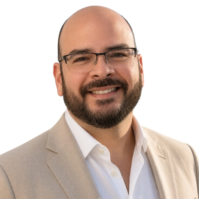 Alberto Labrada, Broker-Owner of Labrada Realty, smiling in a beige suit and glasses.