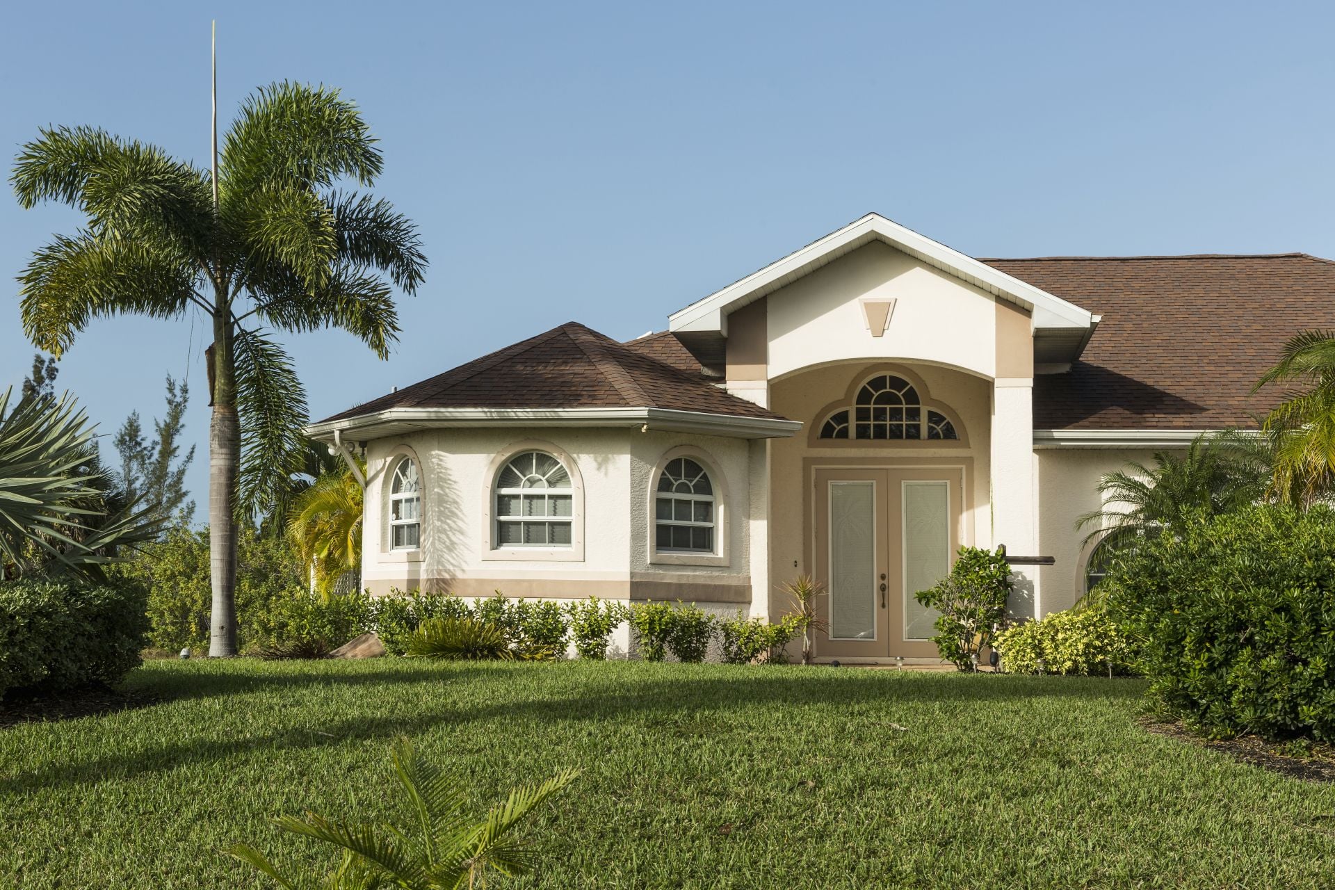 Typical Southwest Florida concrete block and stucco home in the countryside with palm trees, tropical plants and flowers, grass lawn and pine trees. Florida