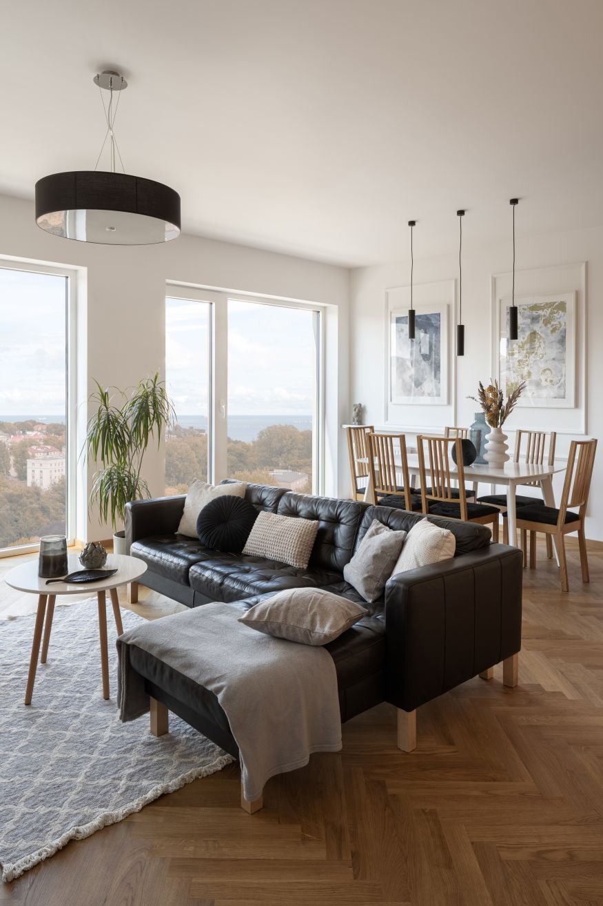 Spacious living room with dining table, comfortable, black corner sofa and big windows