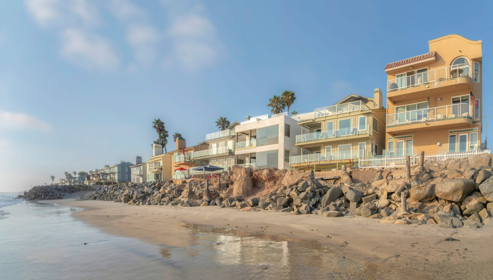 07-14-2021 Carlsbad, California- Beach houses near the rocks sea wall. Oceanside row of beachfront houses with balconies near the shore against the sky background.