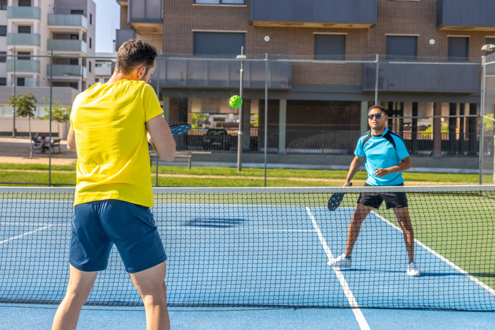 Two men playing pickleball on a blue court, hitting the ball over the net