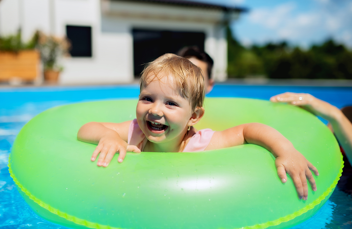 Young family with small daughter in swimming pool outdoors in backyard garden.