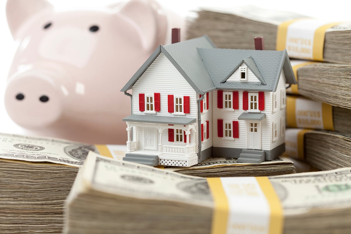 Small House and Piggy Bank with Stacks of Hundred Dollar Bills Isolated on a White Background.