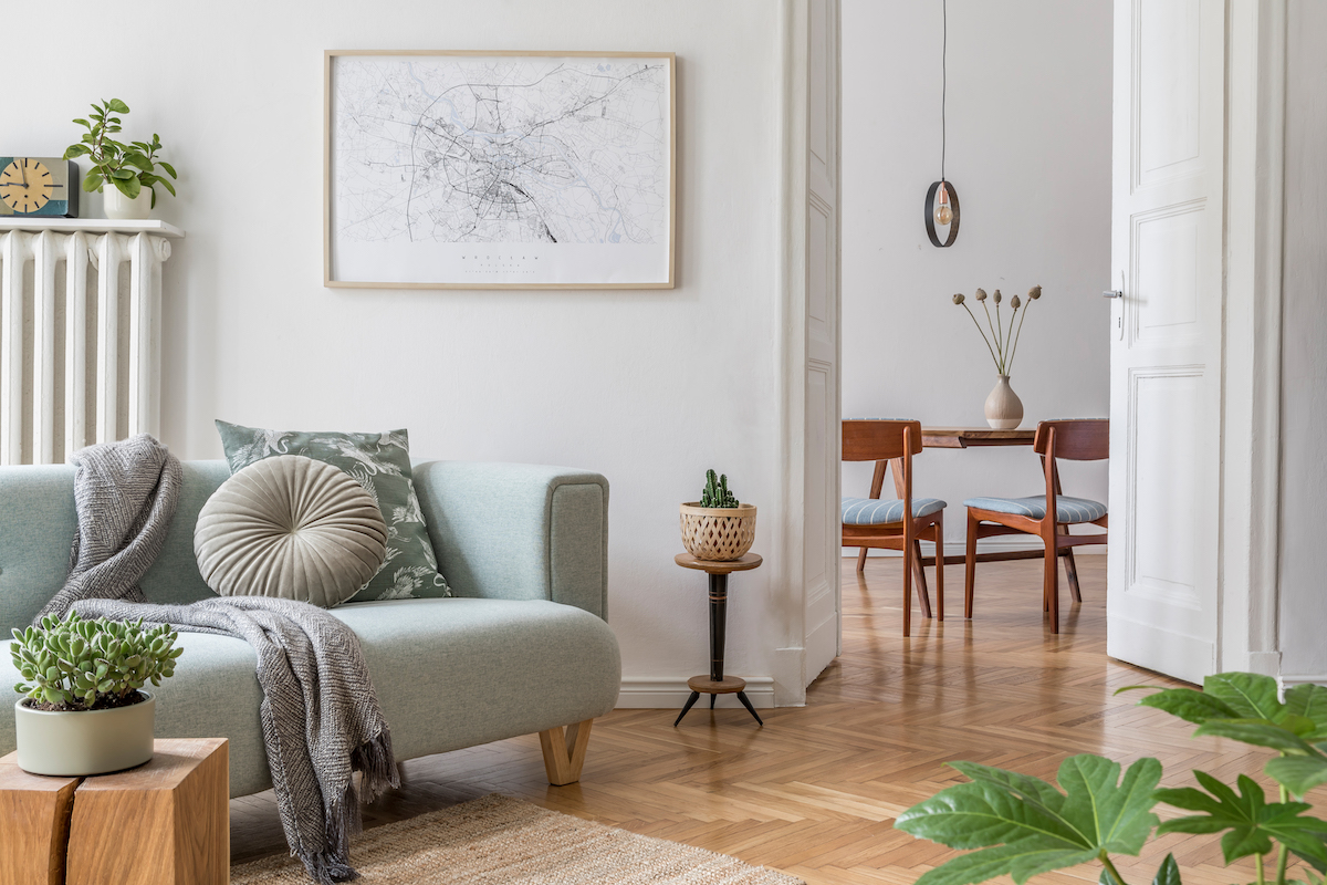 Cozy and creative composition of stylish living room interior design with mock up poster frame, green sofa, wooden furniture, plants and accessories. White walls, parquet floor. Template.