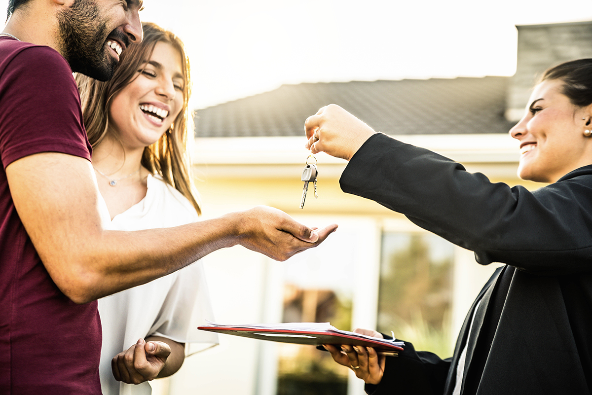 Happy millennial couple receiving keys from realtor, purchasing