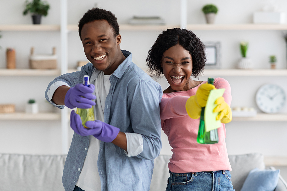 Playful black couple holding detergents during cleaning at home