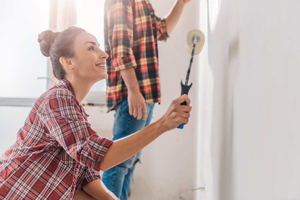smiling young woman holding paint roller and painting wall