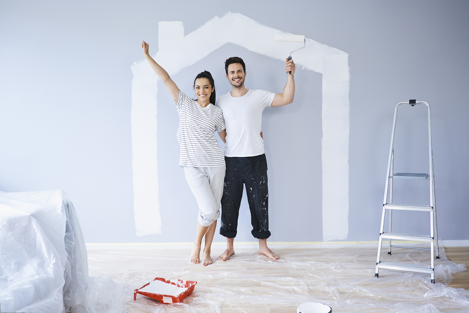 Portrait of cheerful couple painting in new apartment with house shape on wall
