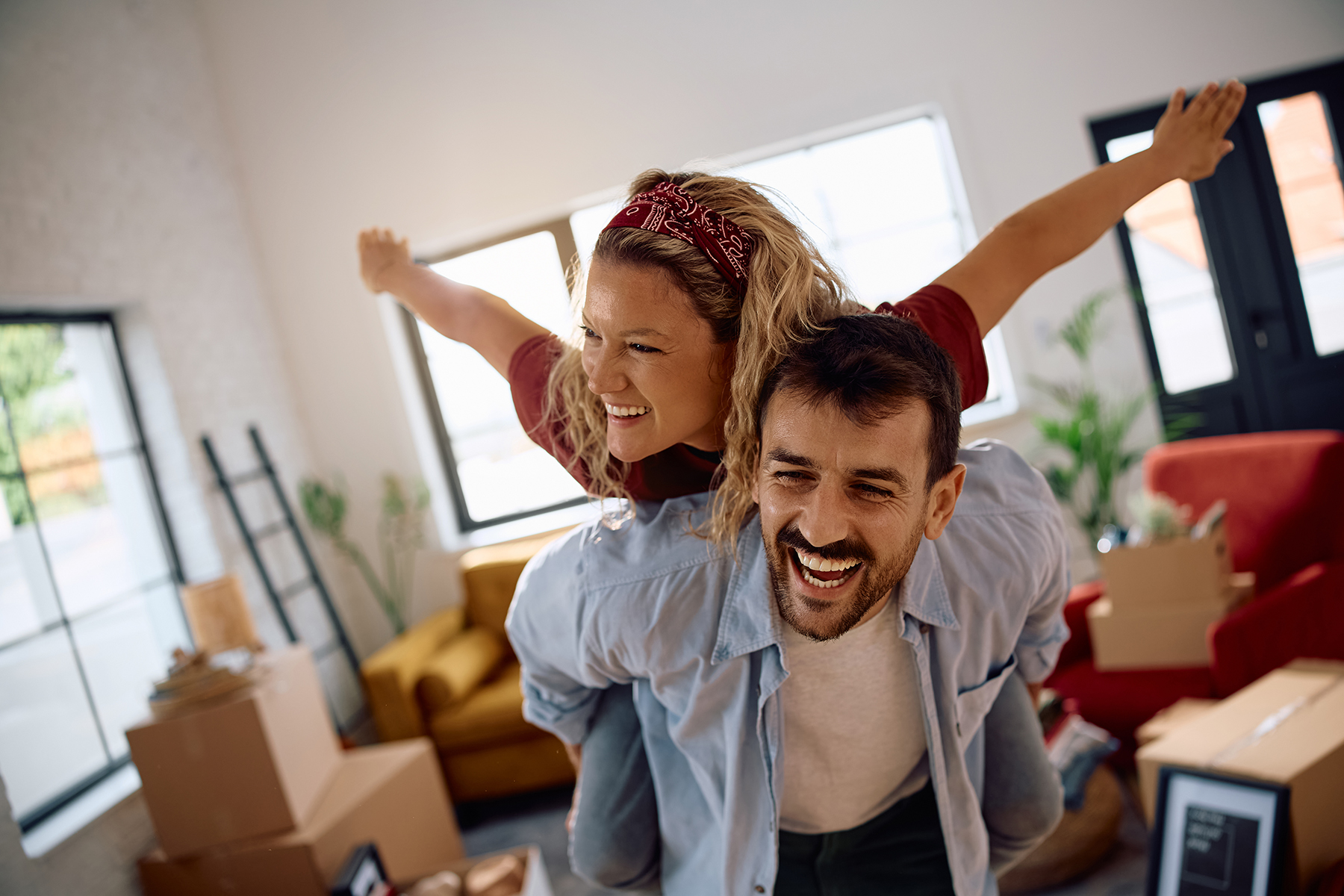 Happy couple having fun and piggybacking while moving into new apartment.