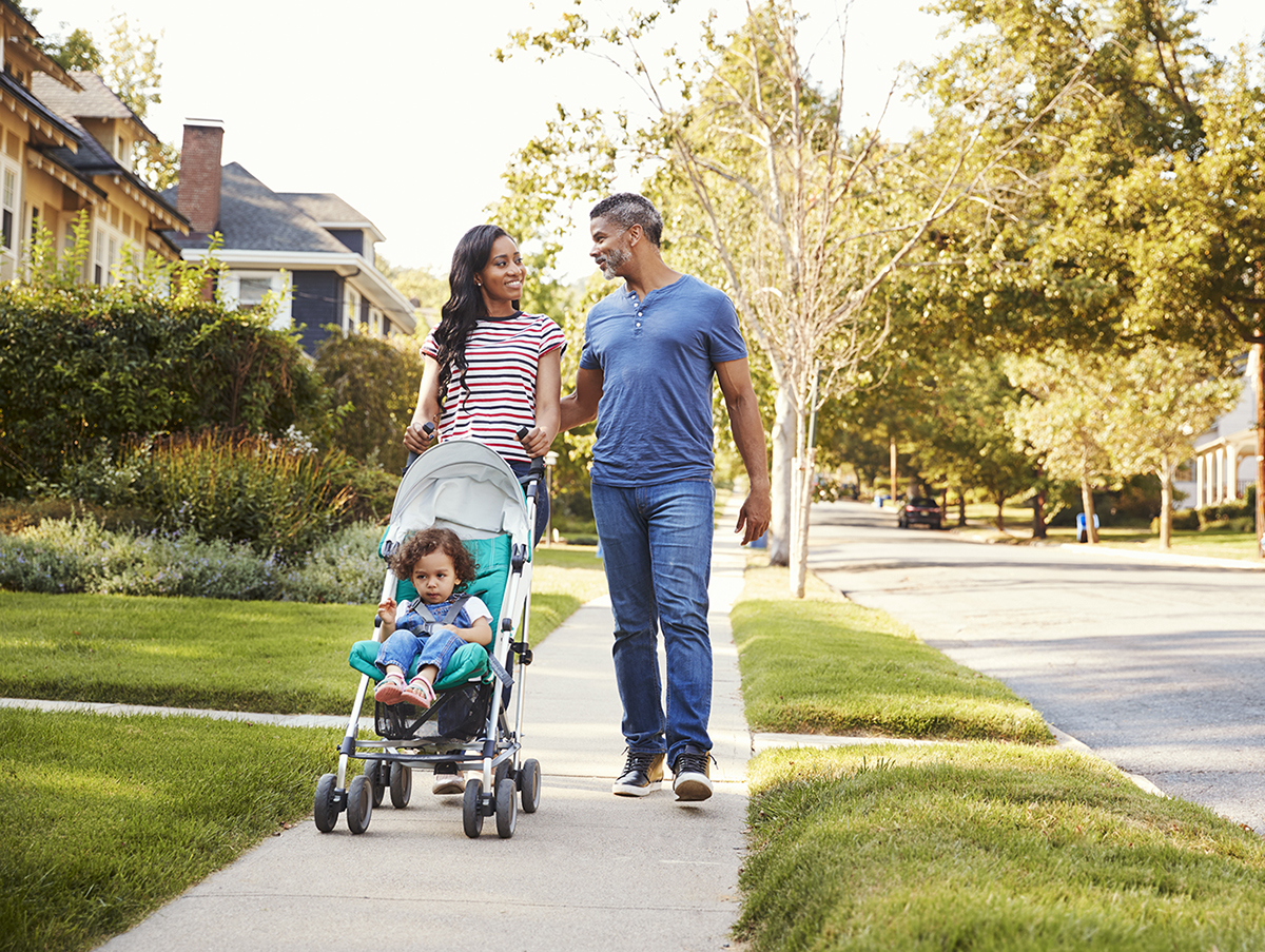 Couple Push Daughter In Stroller As They Walk Along Street