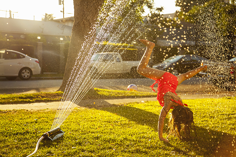 Girl doing handstand under in garden sprinkler