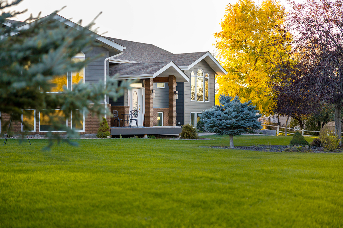 Beautiful two-story house surrounded by lush green grass and tall trees in the backyard