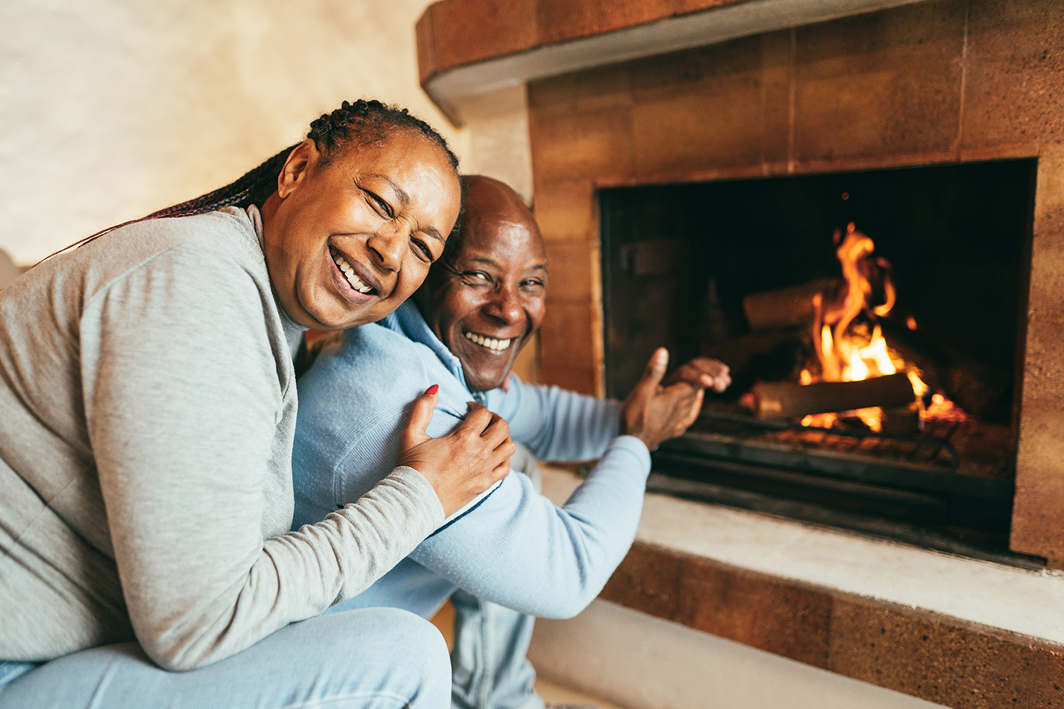 Senior african american couple warming up next to fireplace insi
