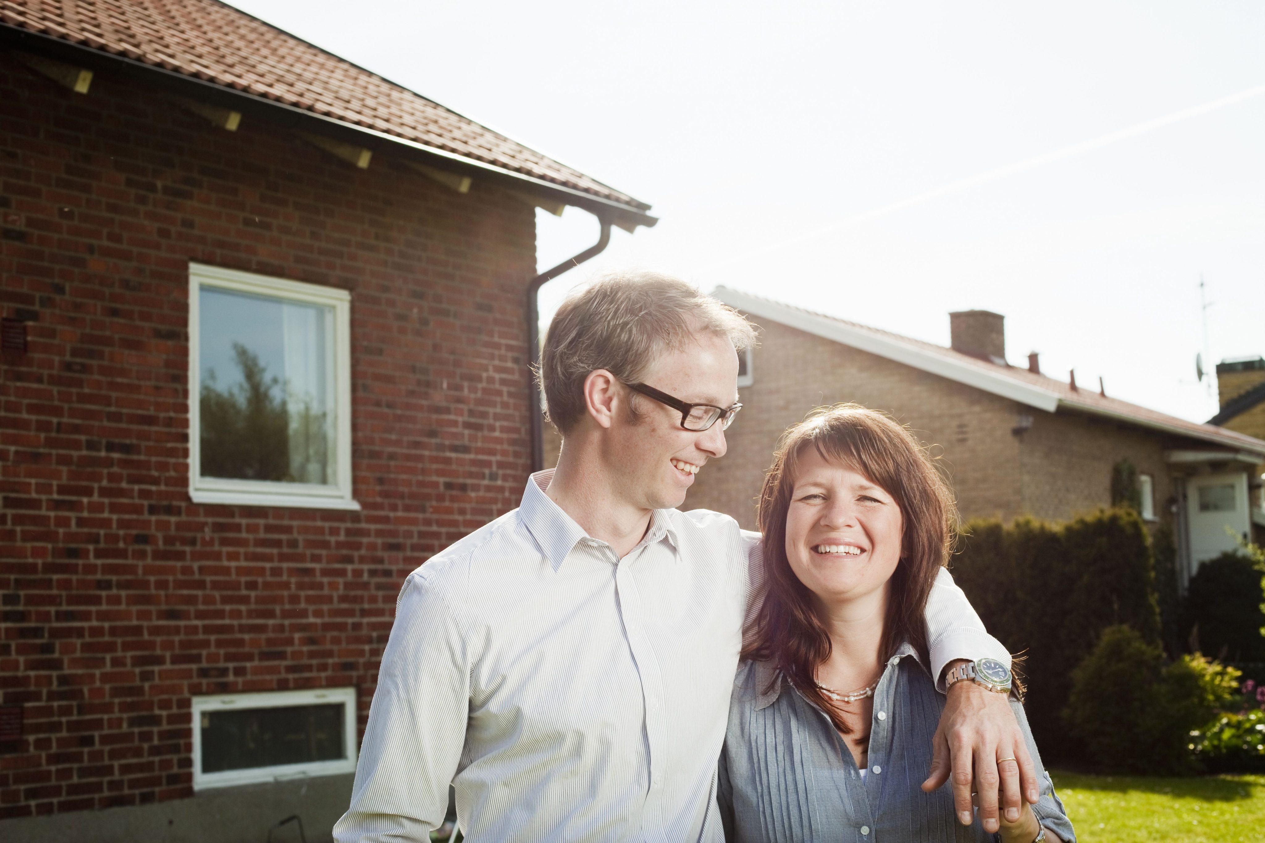 Happy couple standing with arm around in back yard against house