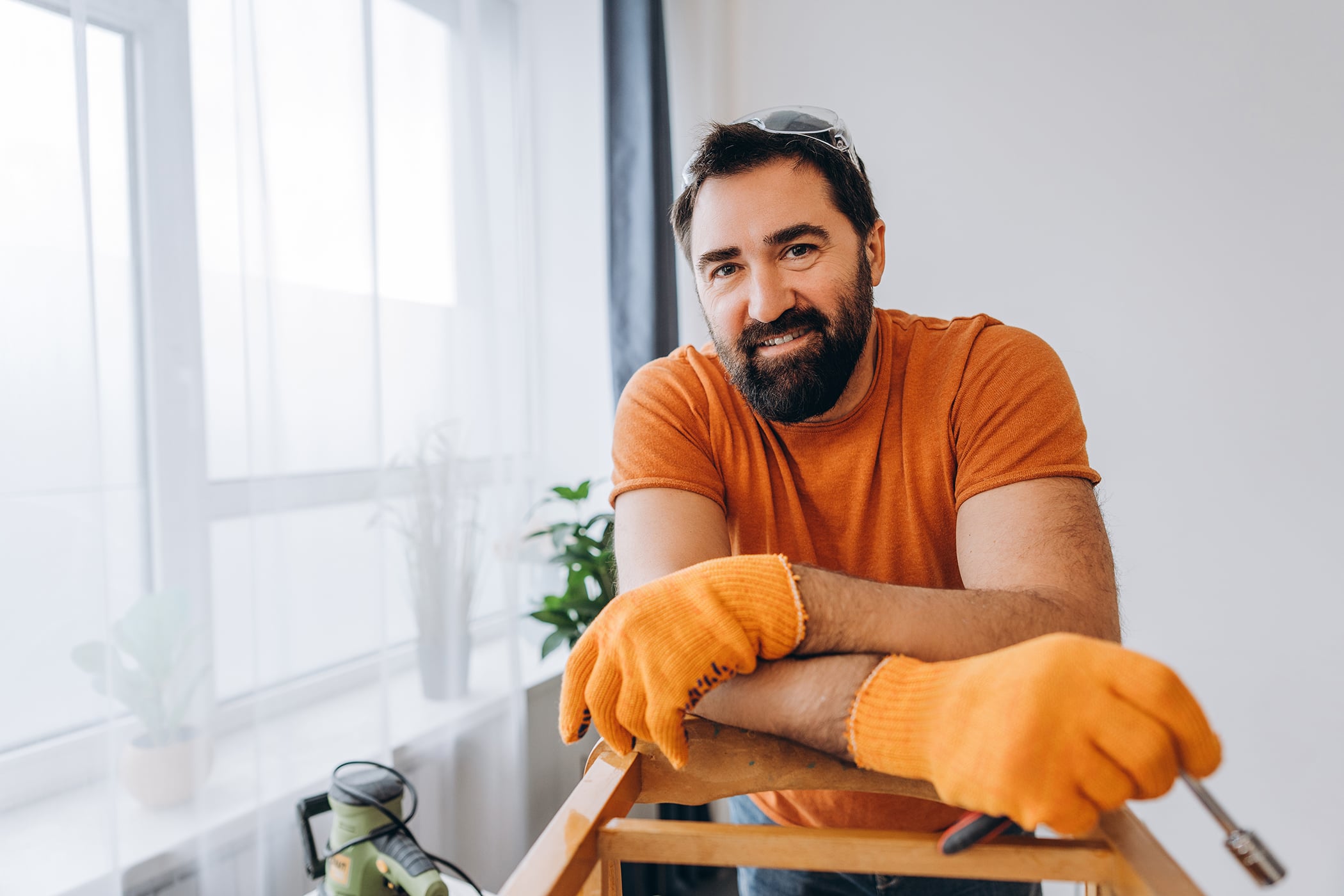 Handsome man smiling while renovating home with tools and wearing gloves
