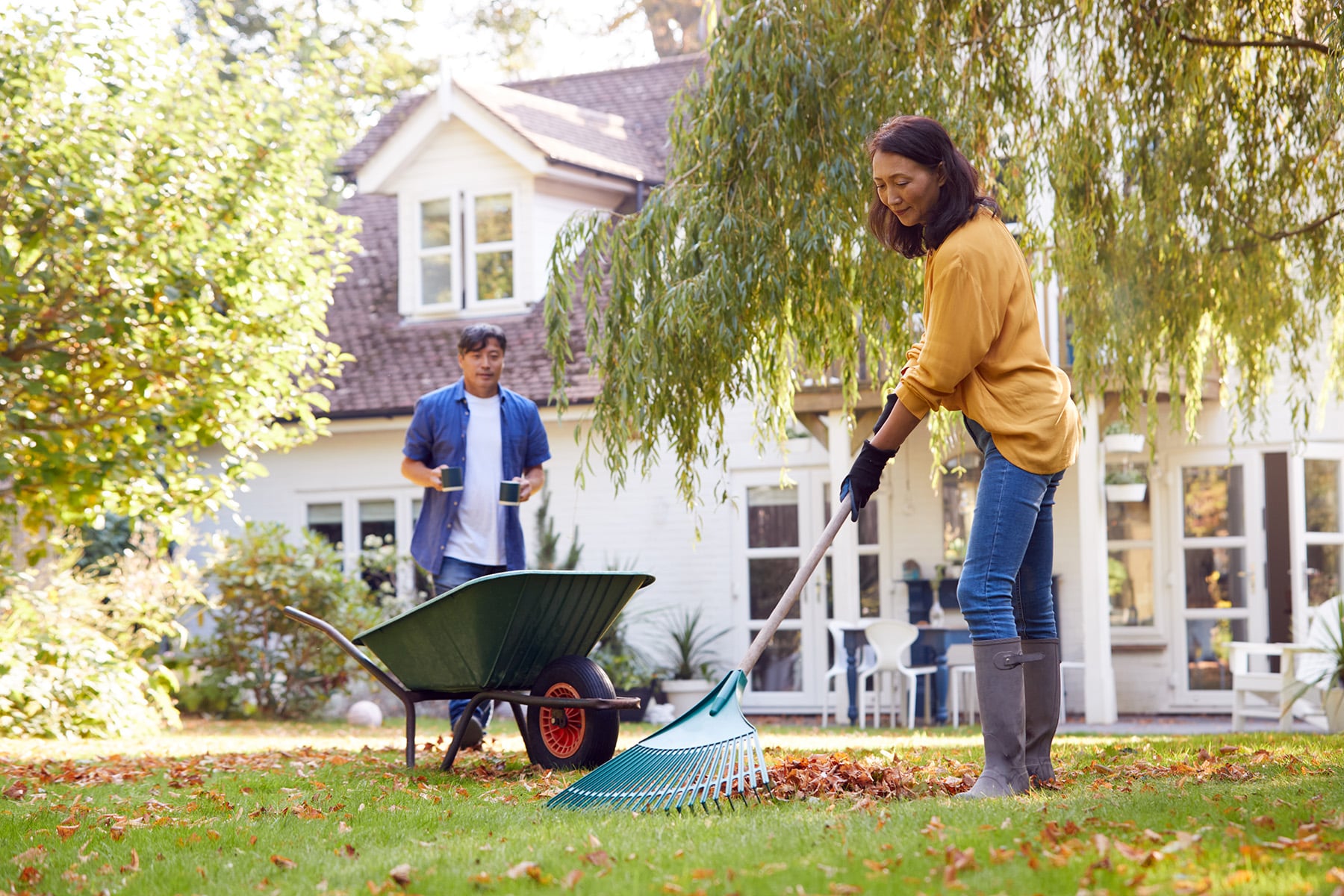 Mature Asian Man Bringing Hot Drink To Woman Tidying Garden With Rake