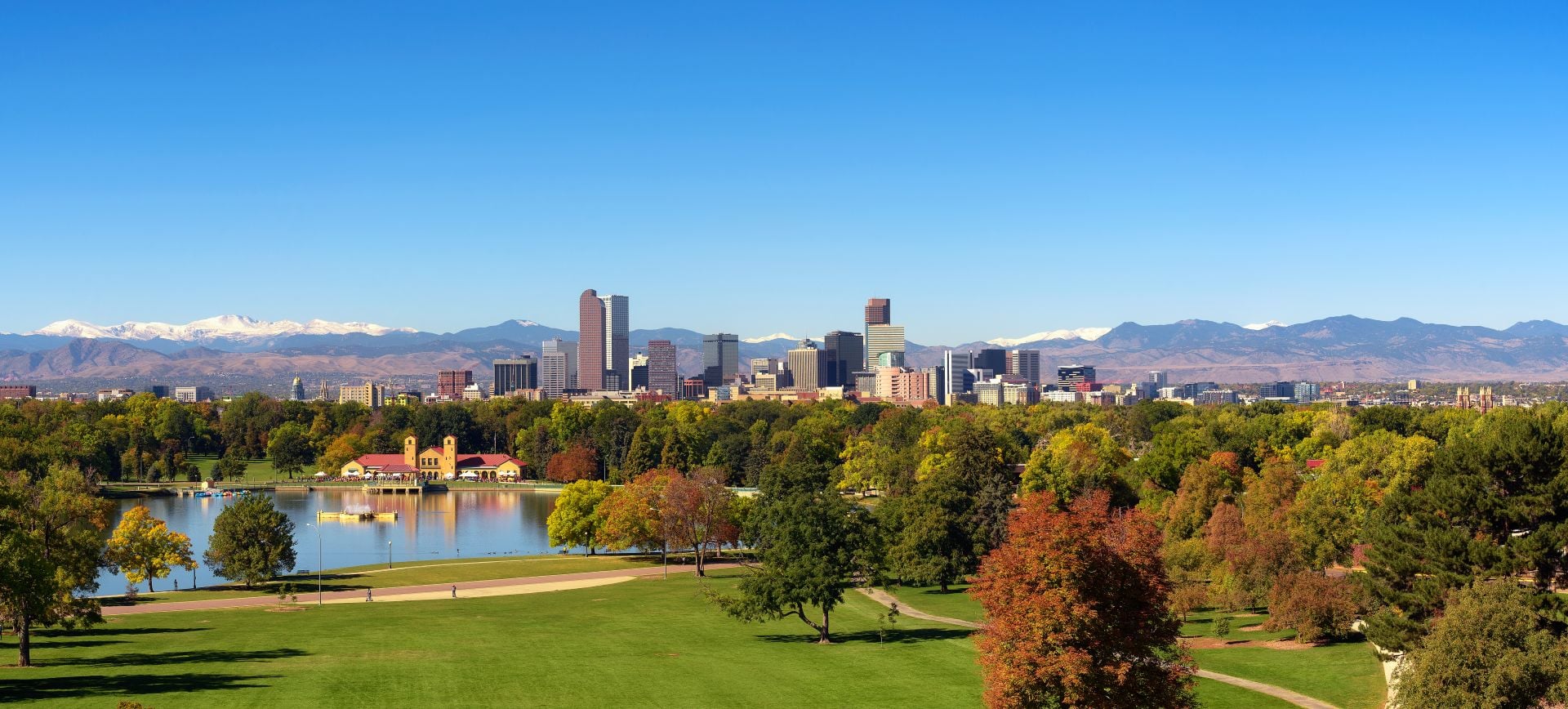 City skyline of Denver Colorado downtown with snowy Rocky Mountains and the City Park Lake. Large panorama.