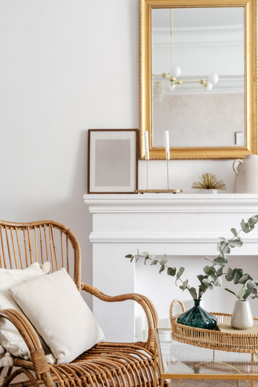 Close up on bamboo rattan armchair with white cushions in modern living room design with home decor in boho chic style. Side table with tray and eucalyptus branch in ceramic vase
