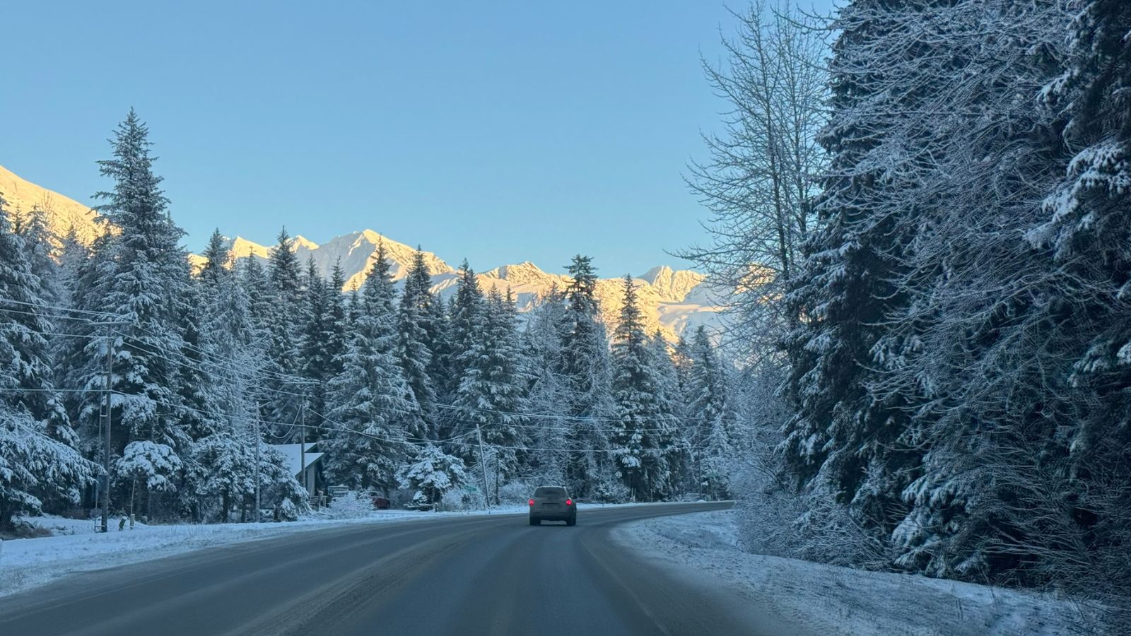 Winter road in Girdwood Alaska with snowy trees and mountains in the background