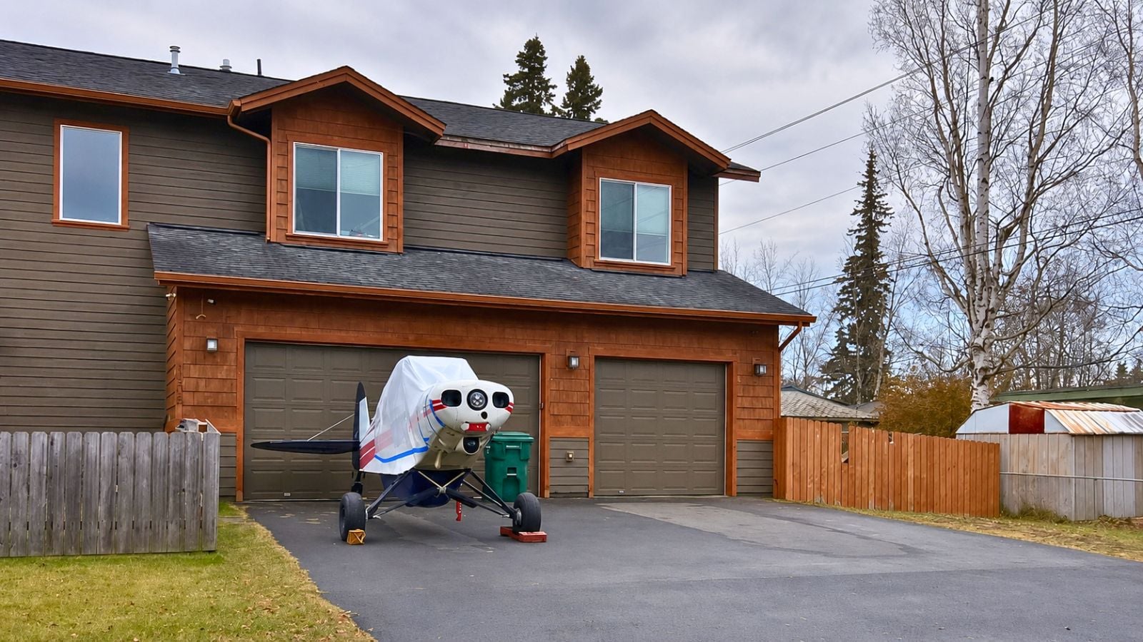Small plane parked in the driveway of an Anchorage home with garages and trees