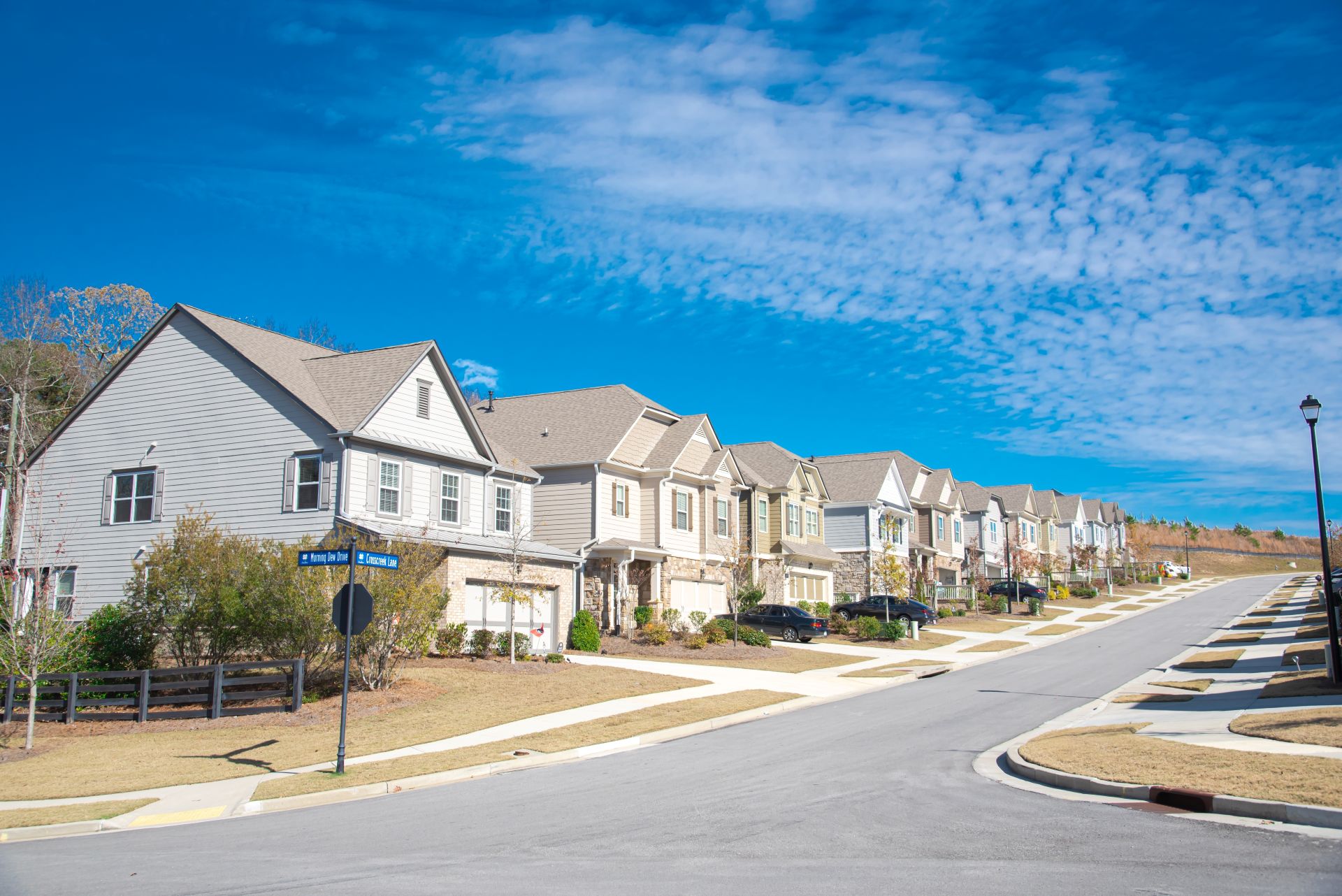 Row of new development two story houses with front garage driveway, well-trimmed landscape and large residential street suburbs of Atlanta, Georgia, USA, sunny blue cloud sky. Subdivision HOA area