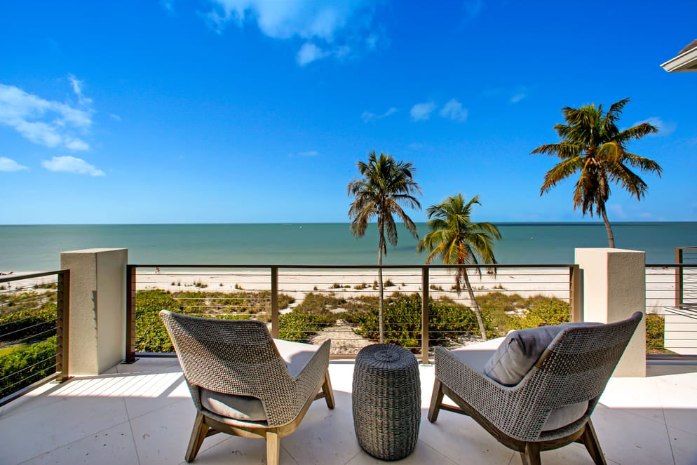 Two chairs on a balcony overlooking the beach in Florida with a grass covered backyard and sand beyond