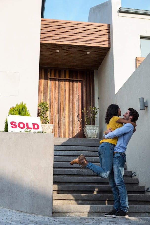 Happy Hispanic couple hugging in front of new house