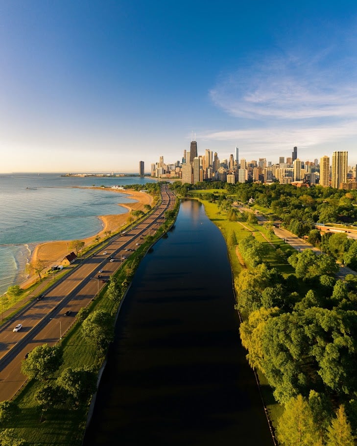 Drone view of Chicago's lakefront with the skyline, beach, and canal captured at golden hour from above.