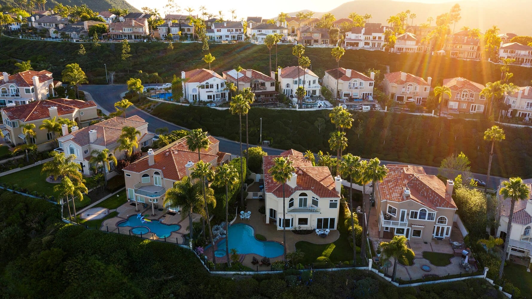 Aerial view of a Southern California neighborhood of tile-roof homes with pools at sunset