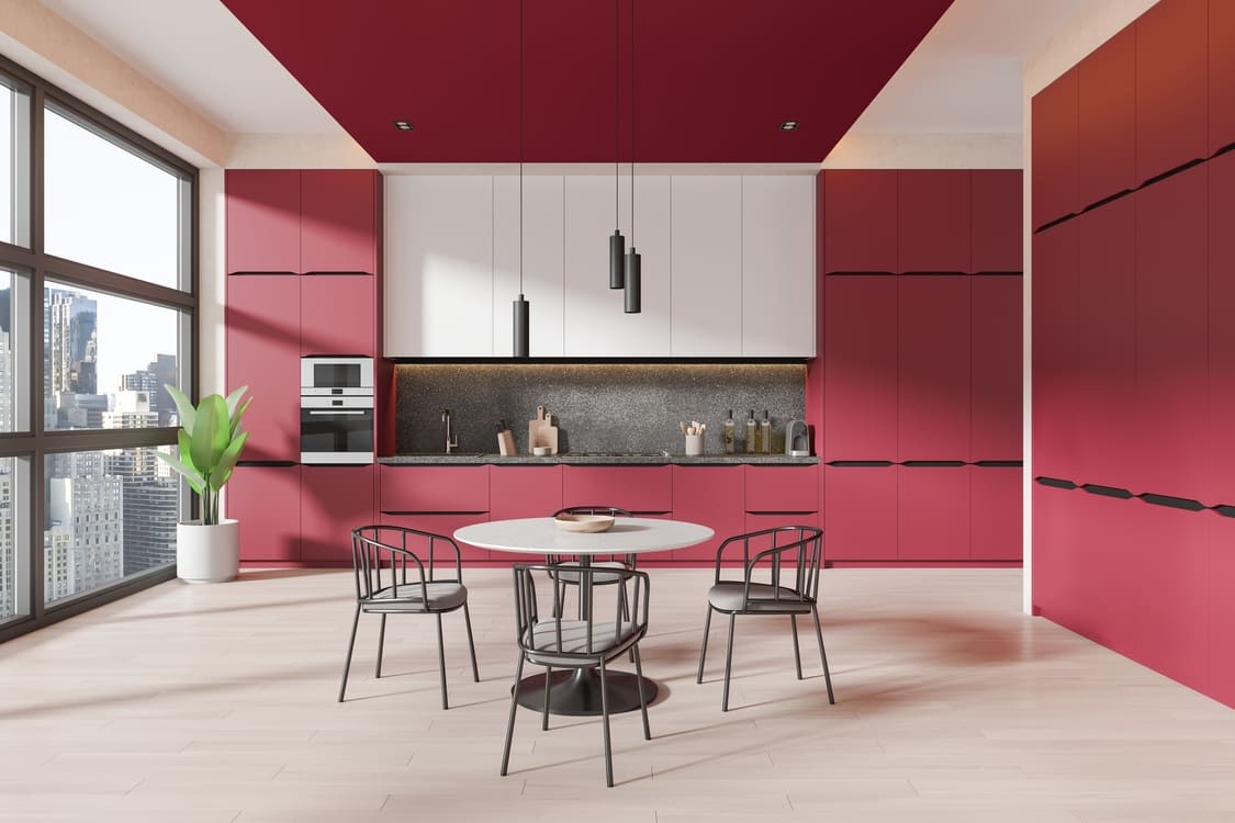 Interior of stylish kitchen with red walls, wooden floor, white cupboards, red cabinets and round dining table with chairs. 3d rendering