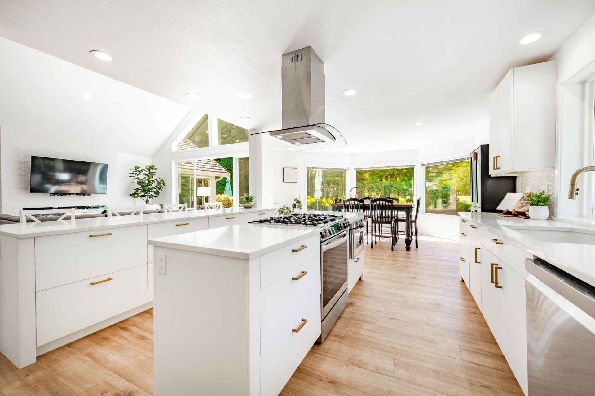 Bright white open concept kitchen with 2 island counters bar stools stainless appliances gold fixtures sink rang hood hardwood floor spacious modern family home interior