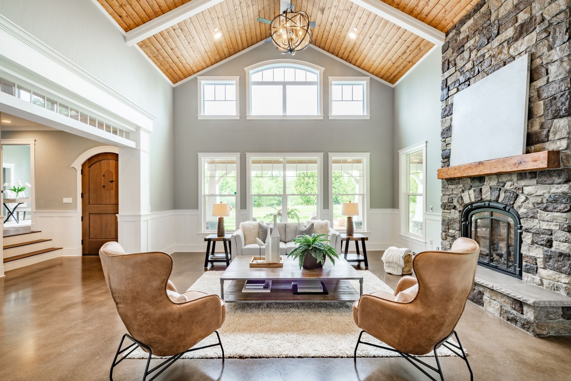 Living room interior with vaulted ceiling with wood cedar panelling stone fireplace brown leather armchairs coffee table and area rug natural brown tones (2)