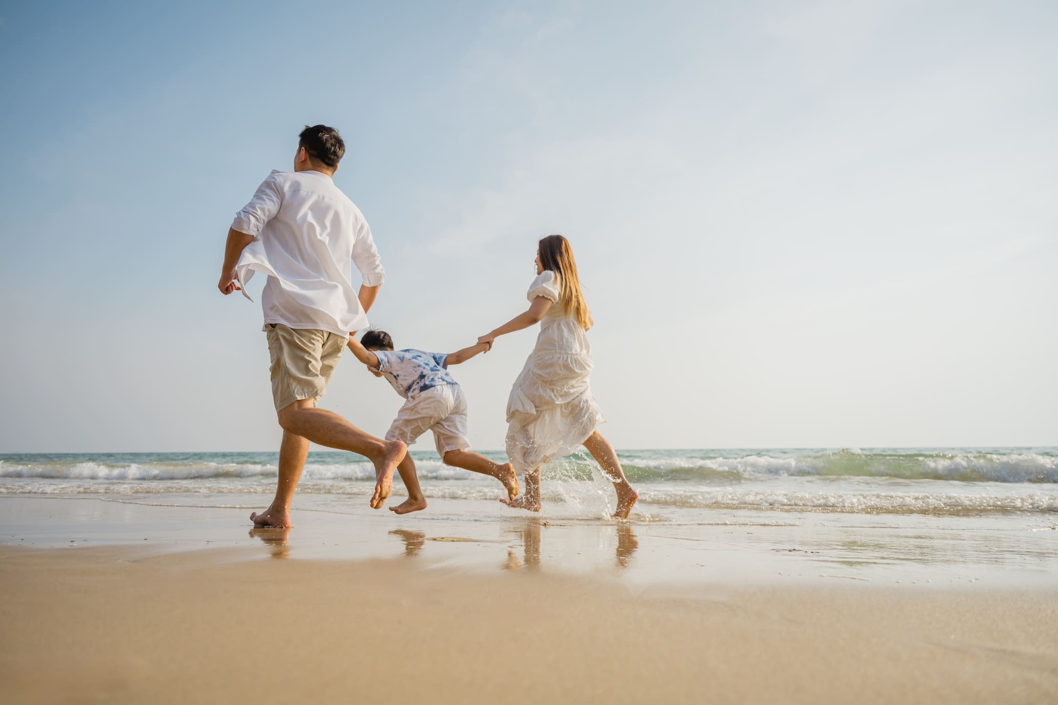 Asian family beach vacation. Children parent relax together. People lifestyle. A family of three, a man, a woman, and a child, are playing on the beach. The man is holding the child's hand.